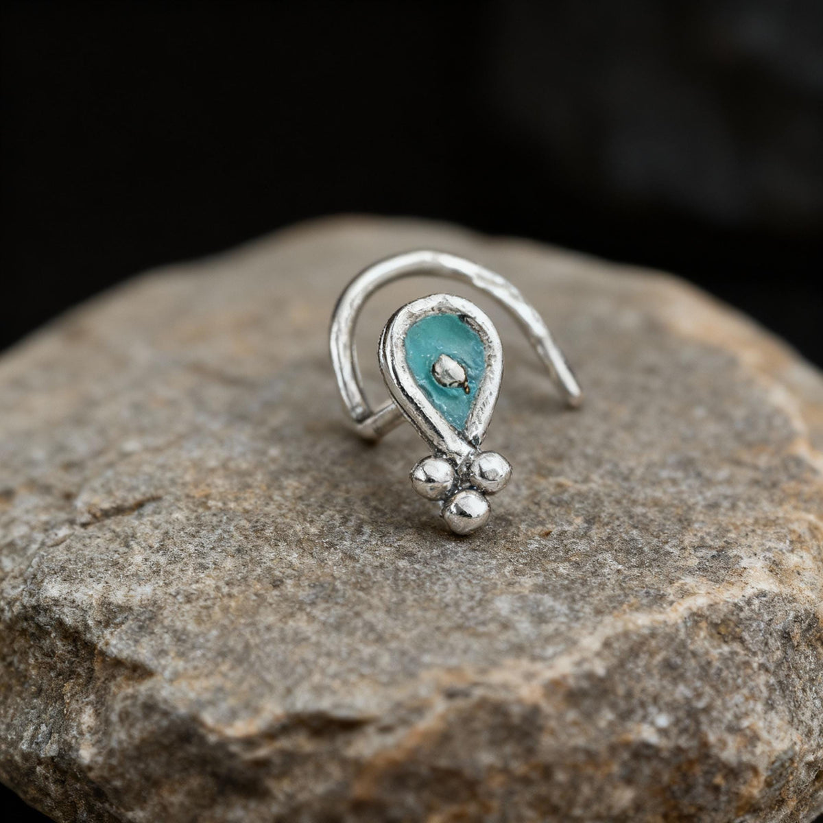 A silver nose ring with a turquoise stone is resting on a rock.