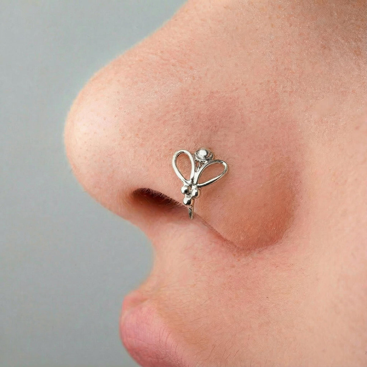 A close-up of a person's nose with a silver butterfly-shaped nose ring.