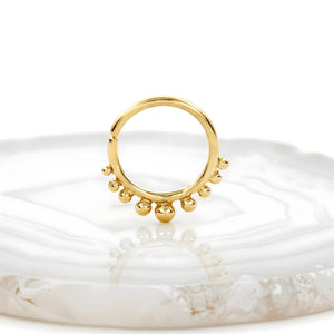 A gold-colored ring with a row of small balls or beads on it, resting on a white surface.