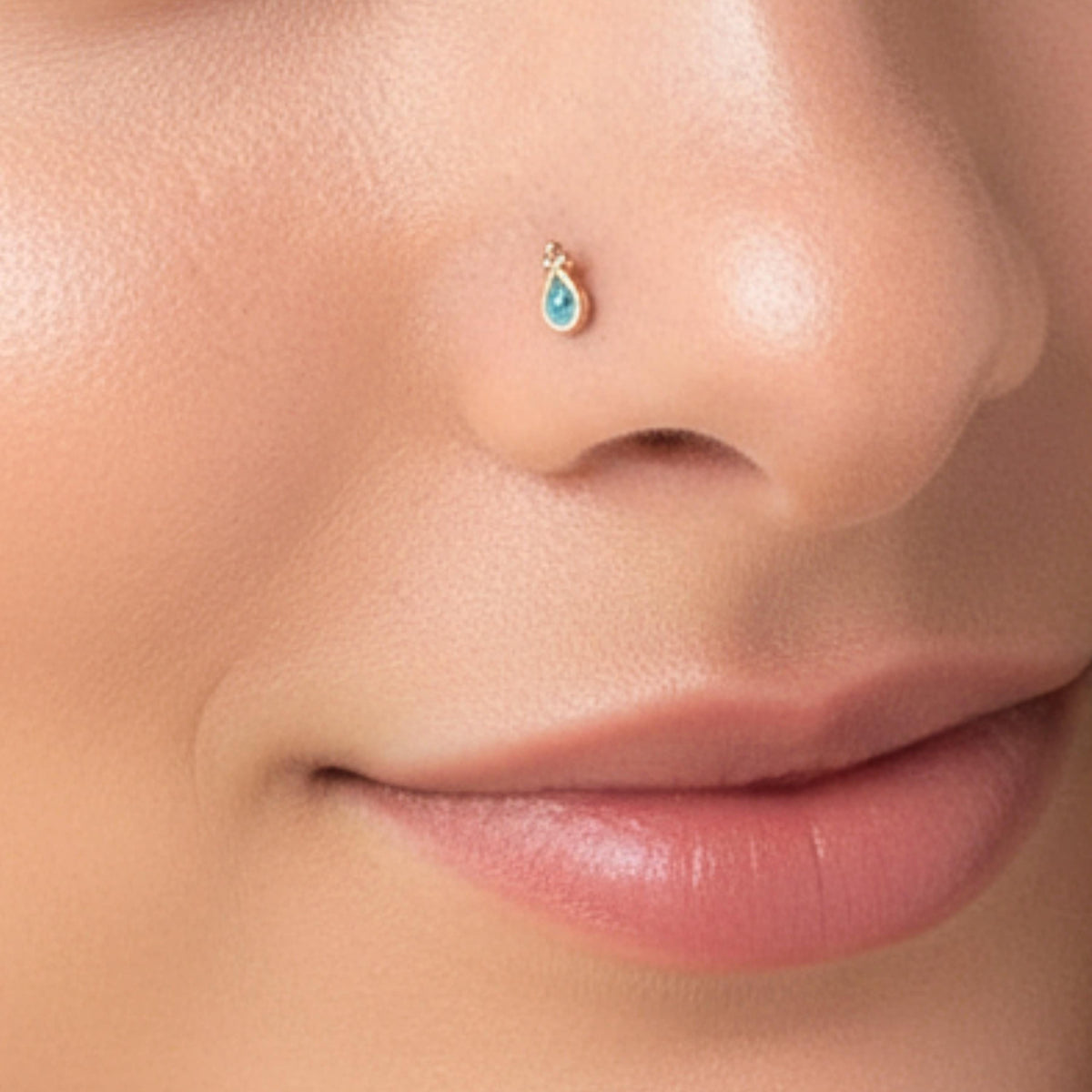 A close-up of a person's nose and mouth, with a small gold nose ring featuring a blue gemstone.