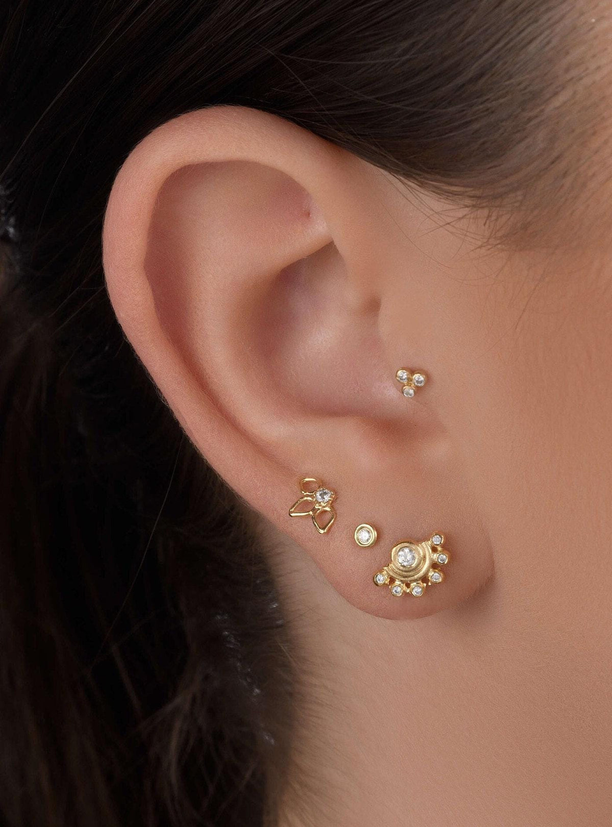 a close-up view of a person's ear adorned with multiple gold earrings.
