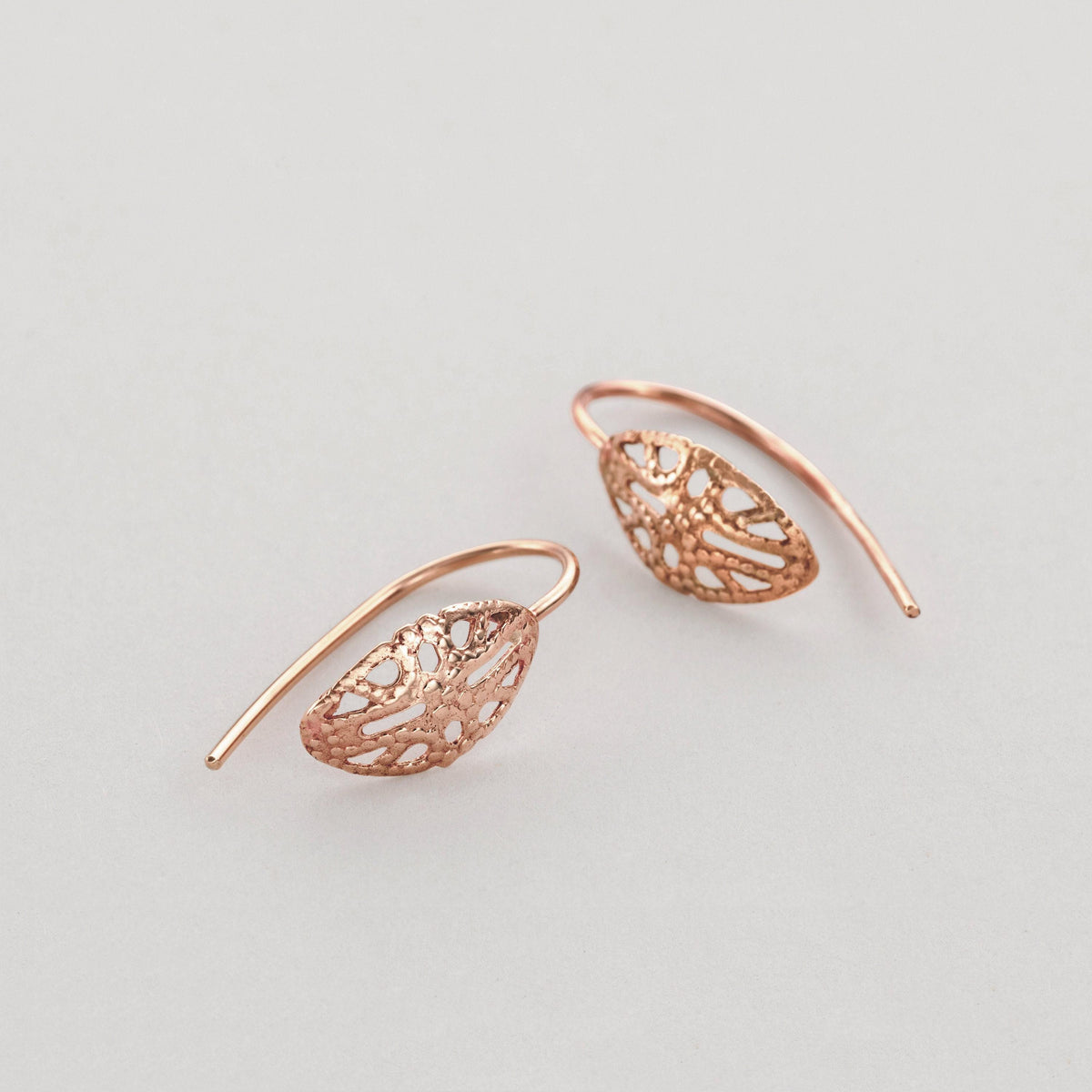A pair of delicate, intricately designed earrings made of a shiny, metallic material, possibly copper or gold, with a floral or leaf-like pattern.