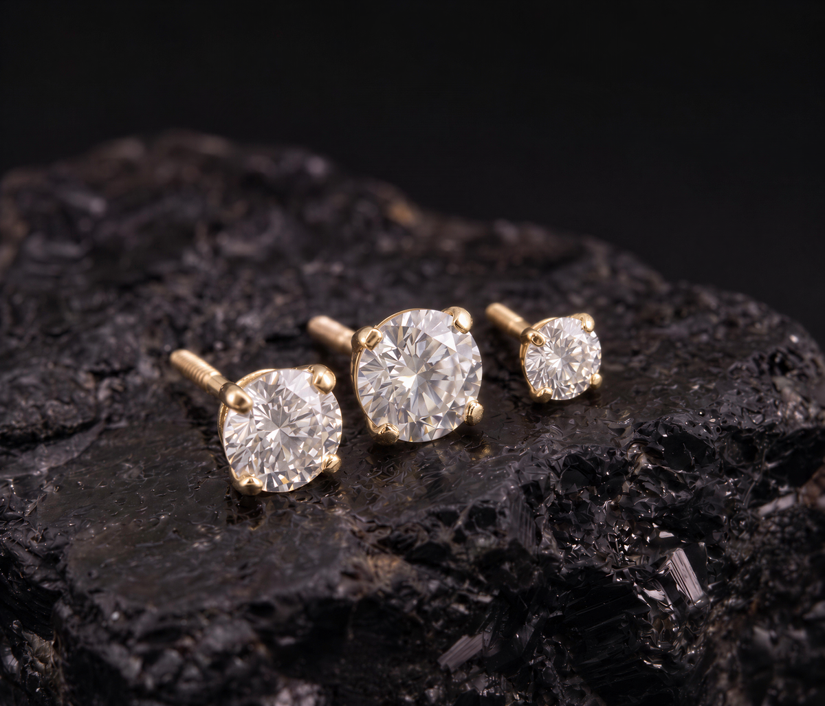 Three gold earrings with large diamonds are displayed on a black rock.
