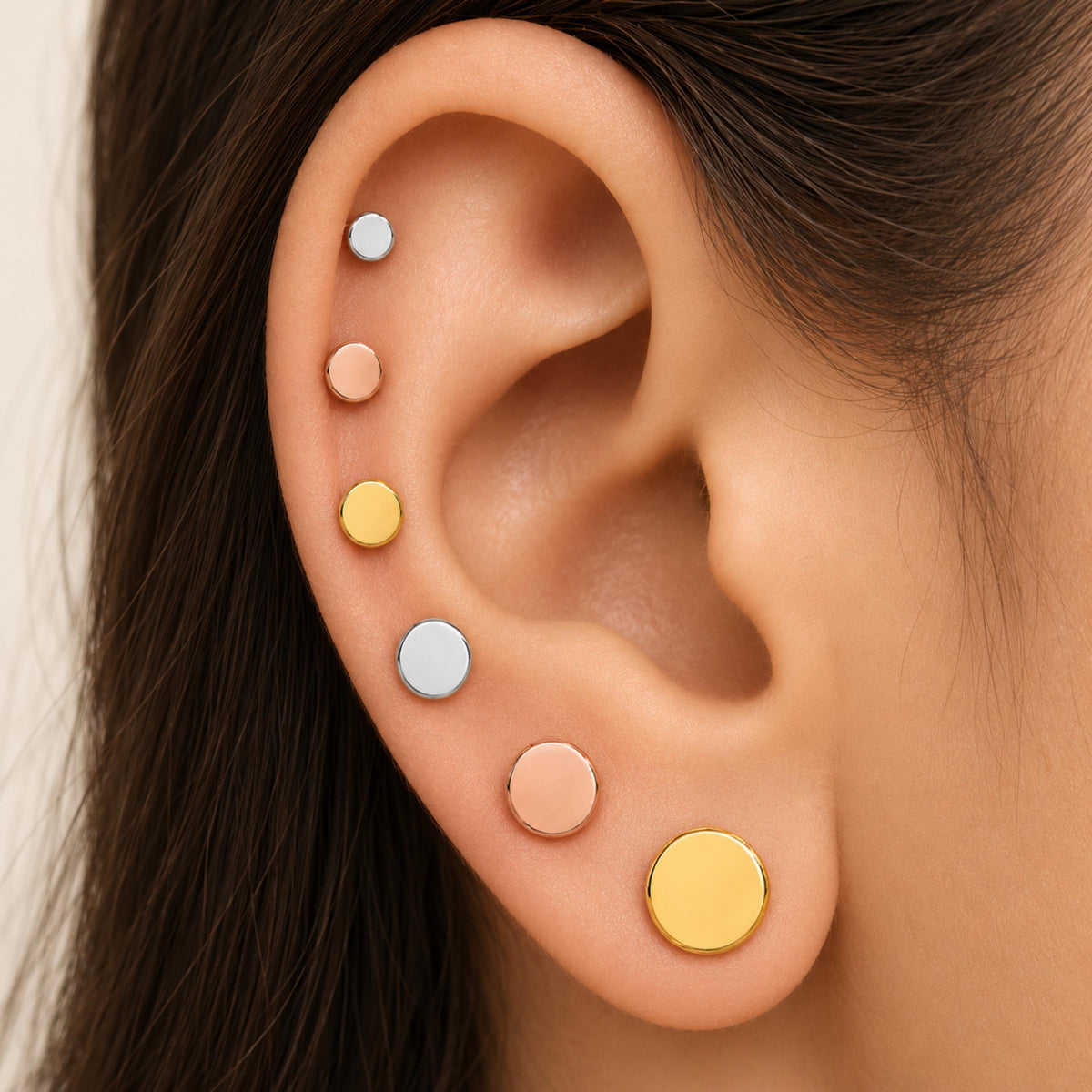 A close-up of a person's ear with multiple round earrings in various colors, including silver, gold, and yellow.
