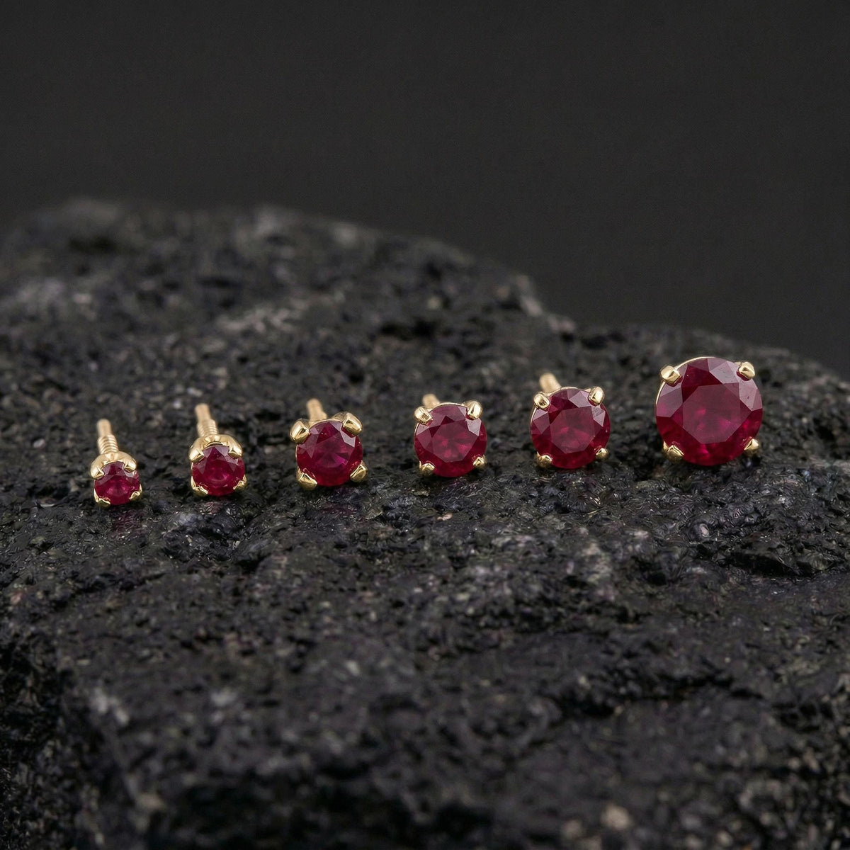 A collection of red gemstone earrings in various sizes, arranged on a dark surface.