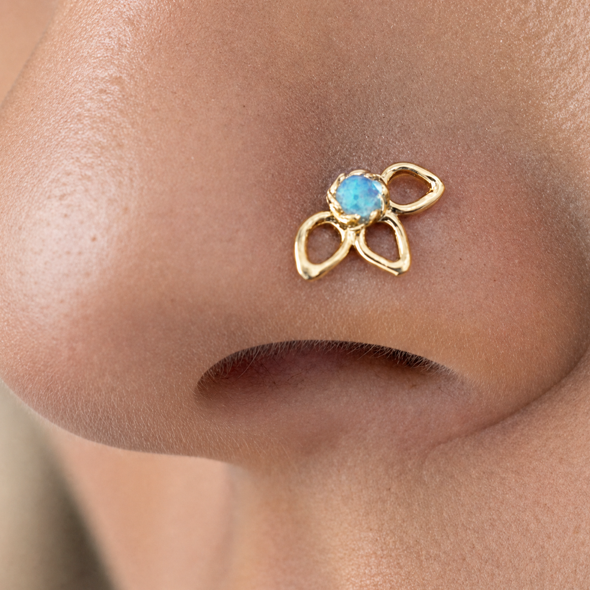 A close-up of a person's nose with a gold-colored nose ring featuring a blue gemstone.
