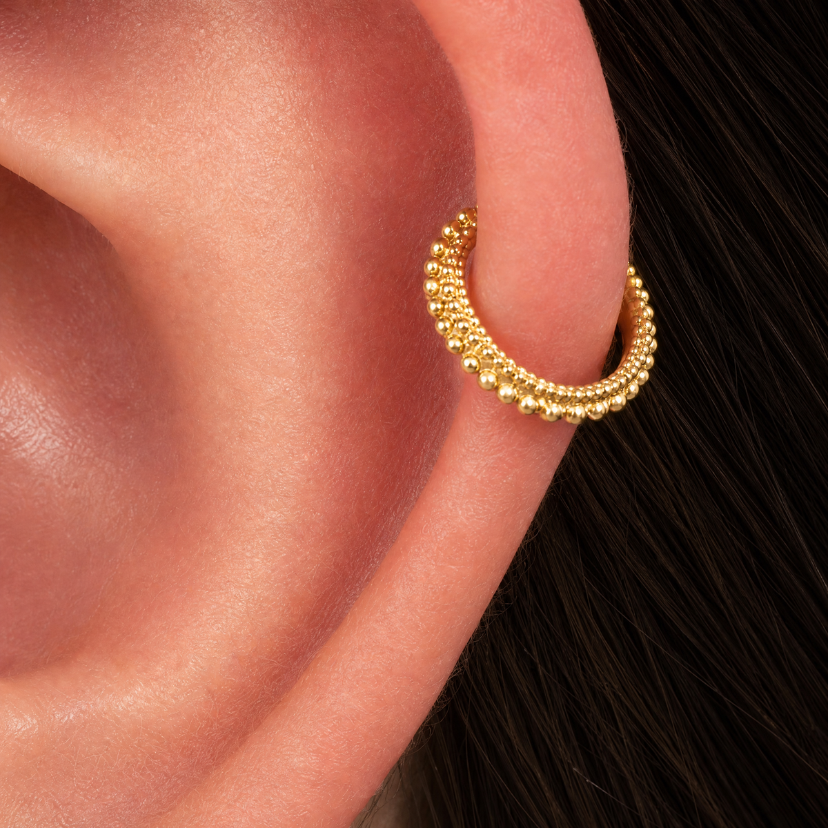 A close-up of a gold earring with a decorative design on the earlobe.