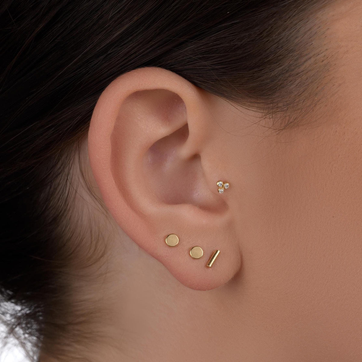A close-up view of a person's ear adorned with a collection of gold earrings, including three circular earrings and a small stud.