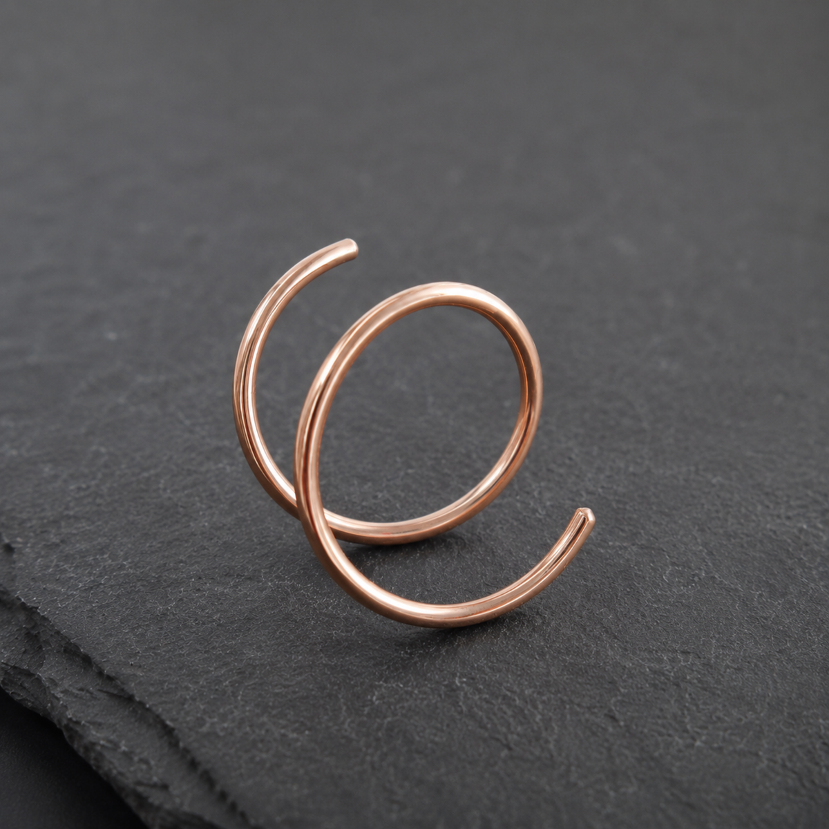 A copper-colored ring with a twisted, coiled design is displayed on a dark surface.