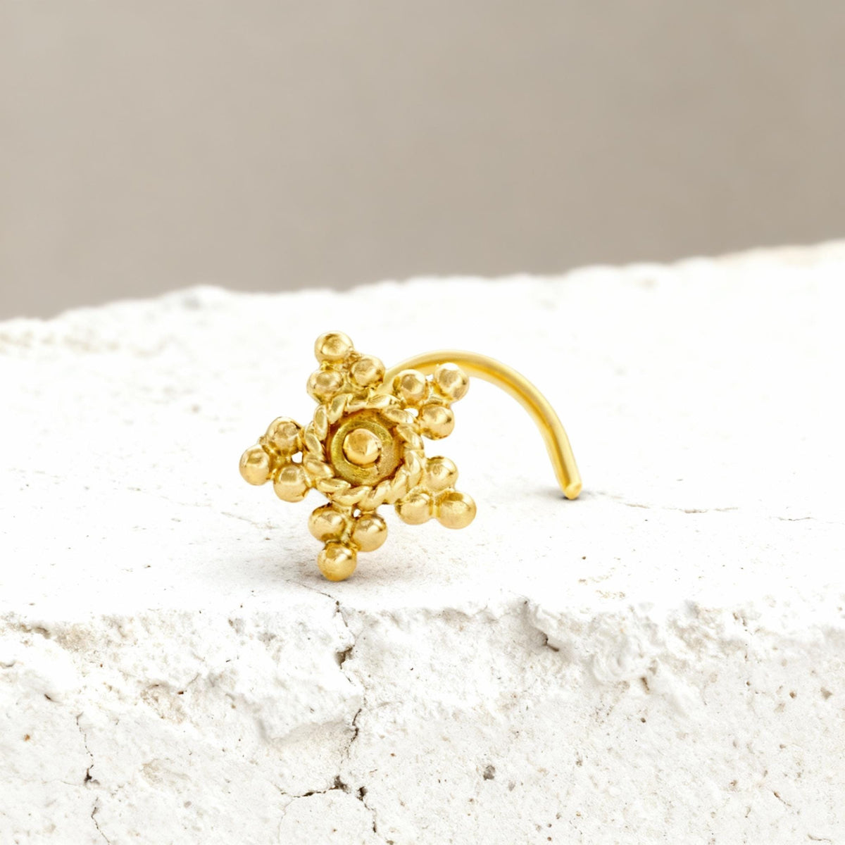 A gold-colored metal nose ring with a star-shaped design and small round balls is displayed on a white surface.