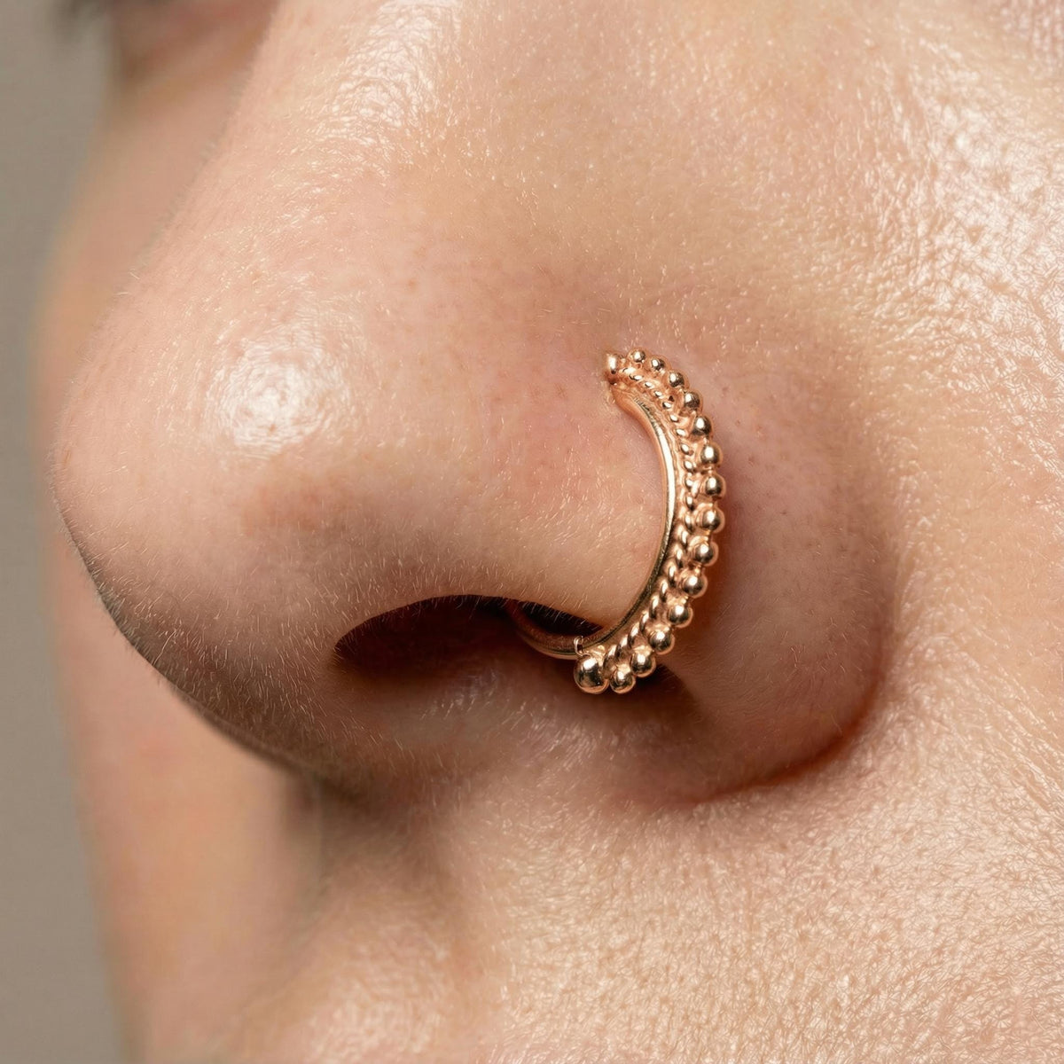 A close-up of a person's nose with a decorative gold nose ring.