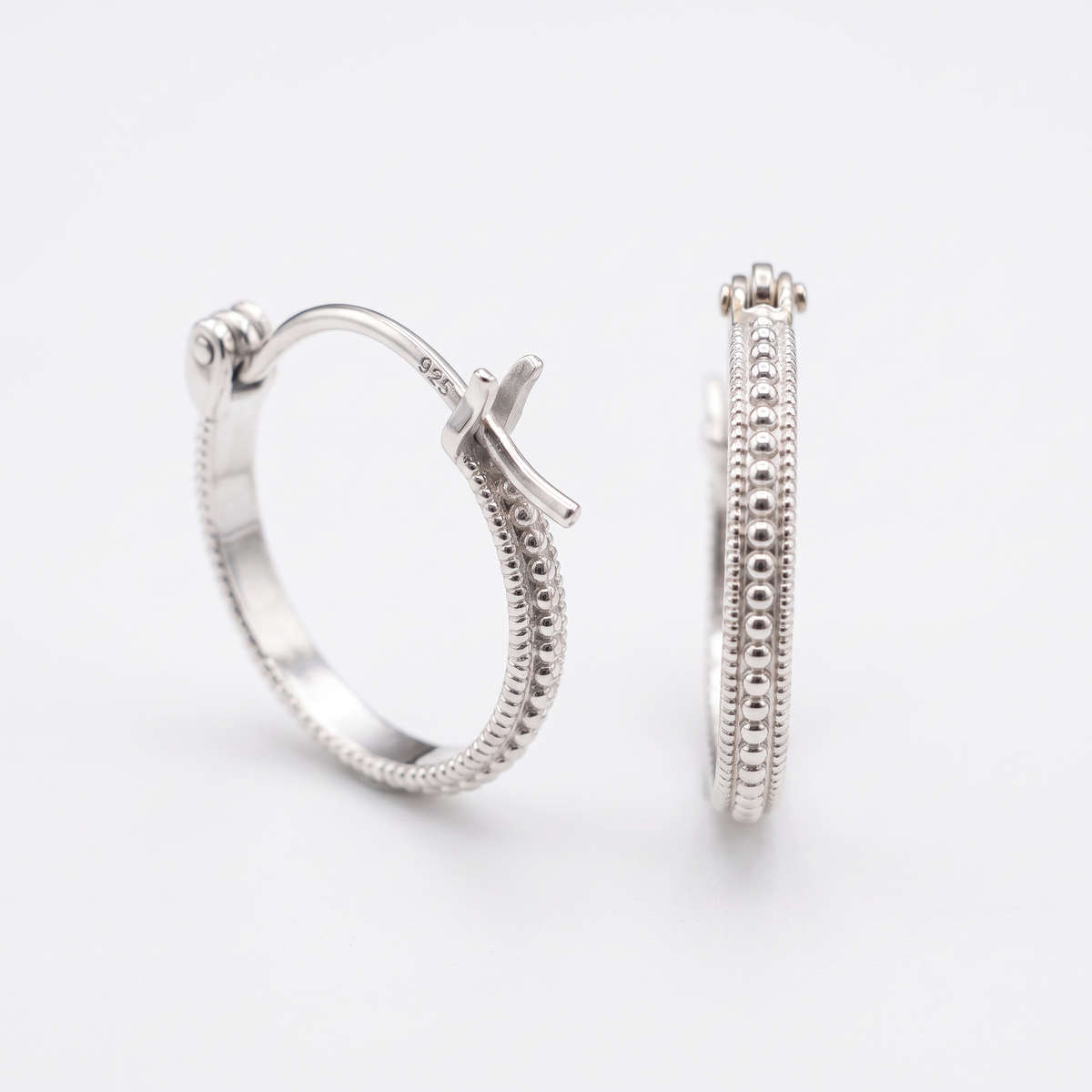 A pair of silver earrings with a cross-shaped clasp and a textured band design.