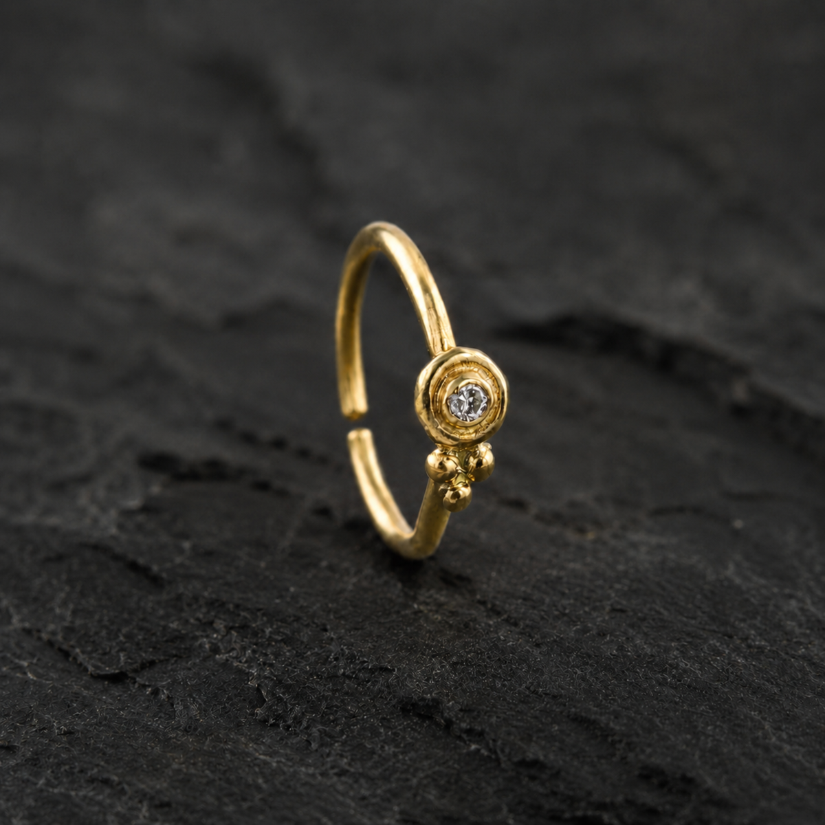 A gold nose ring with a small diamond in the center is displayed against a dark background.