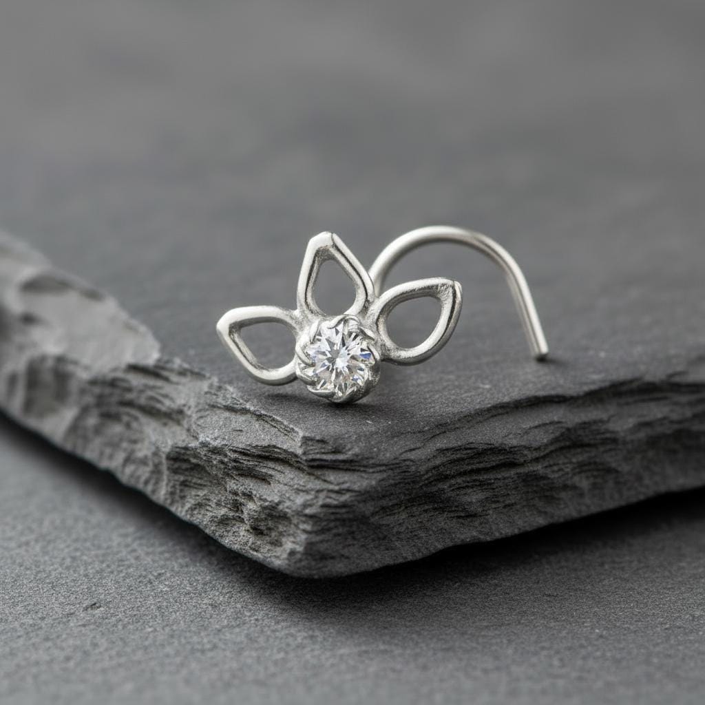 A silver nose ring with a clear gemstone is resting on a gray rock.