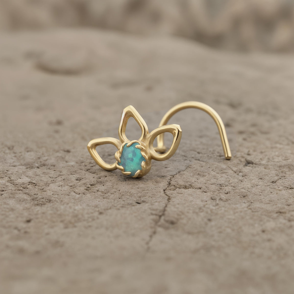 A gold-colored nose ring with a blue gemstone is resting on a rock surface.