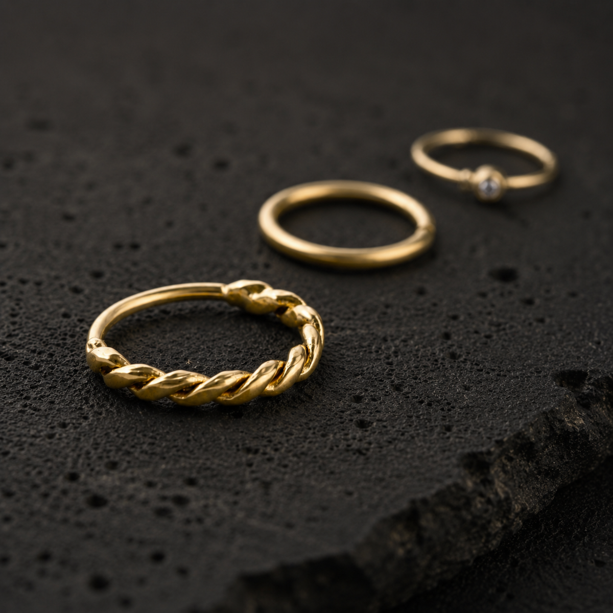 Three gold rings are displayed on a black surface, with the ring in the center being the largest and the other two rings being smaller.