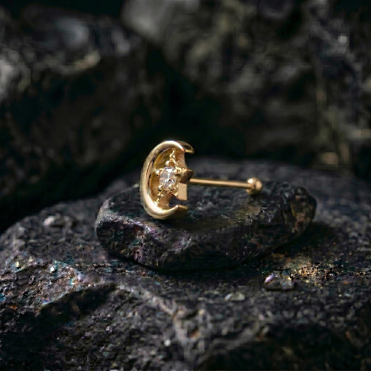 A gold earring with a small gemstone sits on a dark, rocky surface.