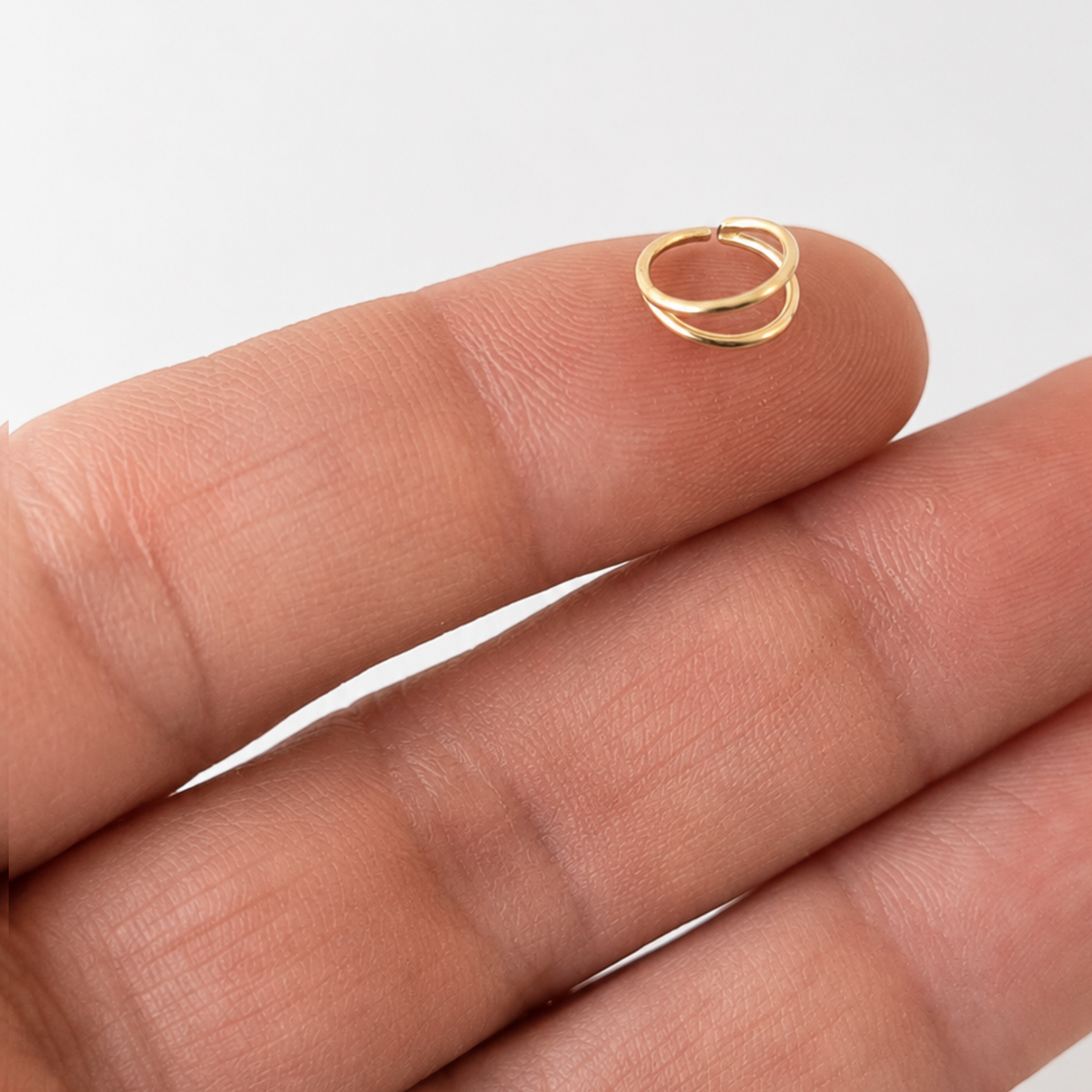 A small gold-colored nose ring is being held in a person's hand.