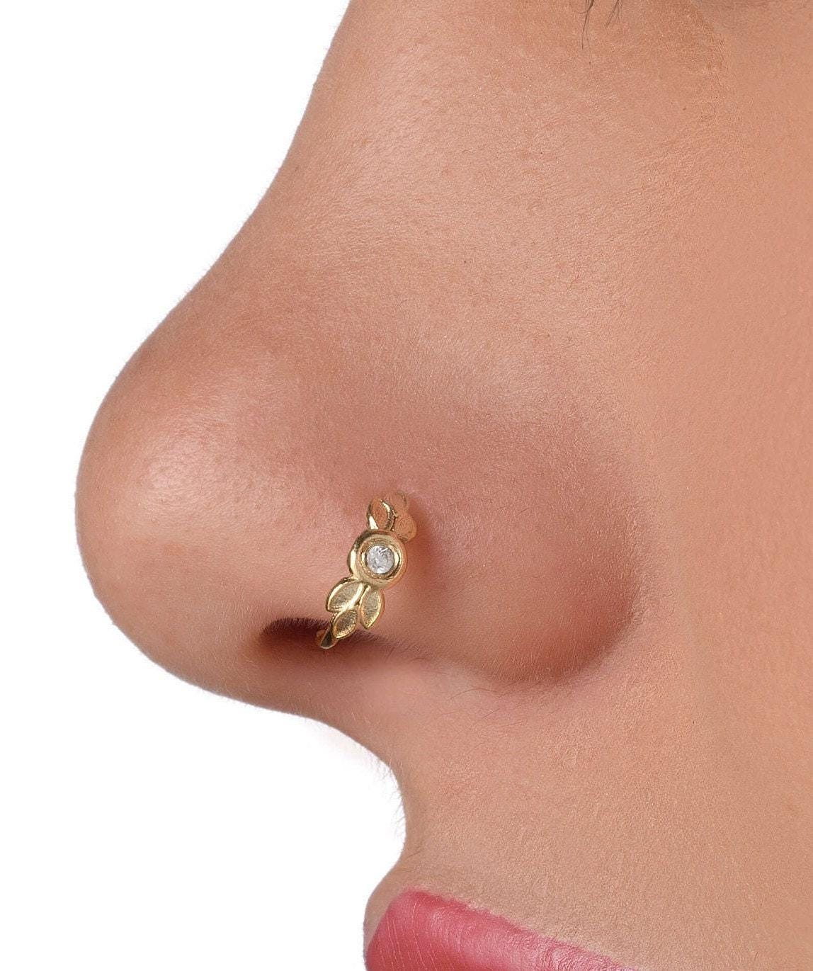 A close-up of a person's nose with a gold-colored nose ring featuring a leaf-shaped design.