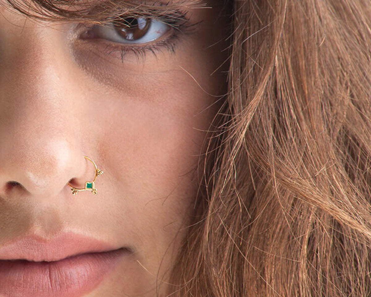 A close-up of a person's face, focusing on their nose and eye, with a nose ring and long, wavy hair.