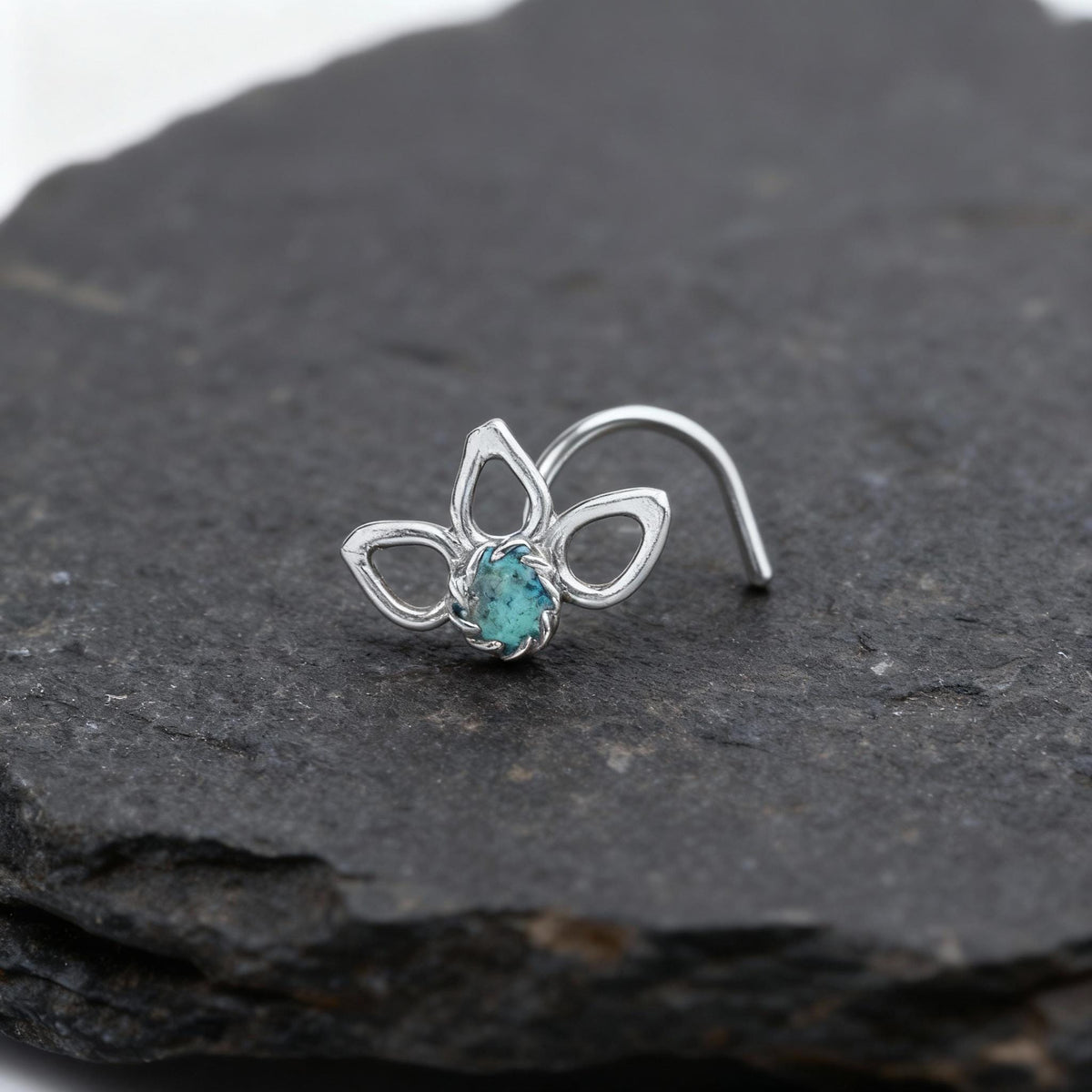 A silver nose ring with a blue gemstone is resting on a dark gray rock.