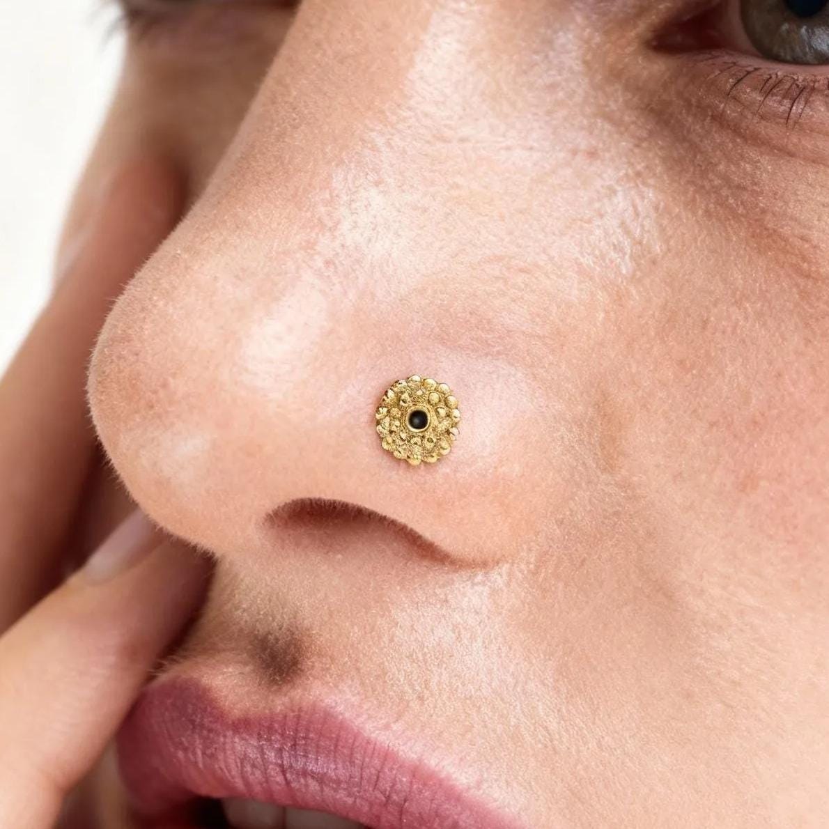 A close-up of a woman's face, focusing on her nose and the gold nose ring she is wearing.