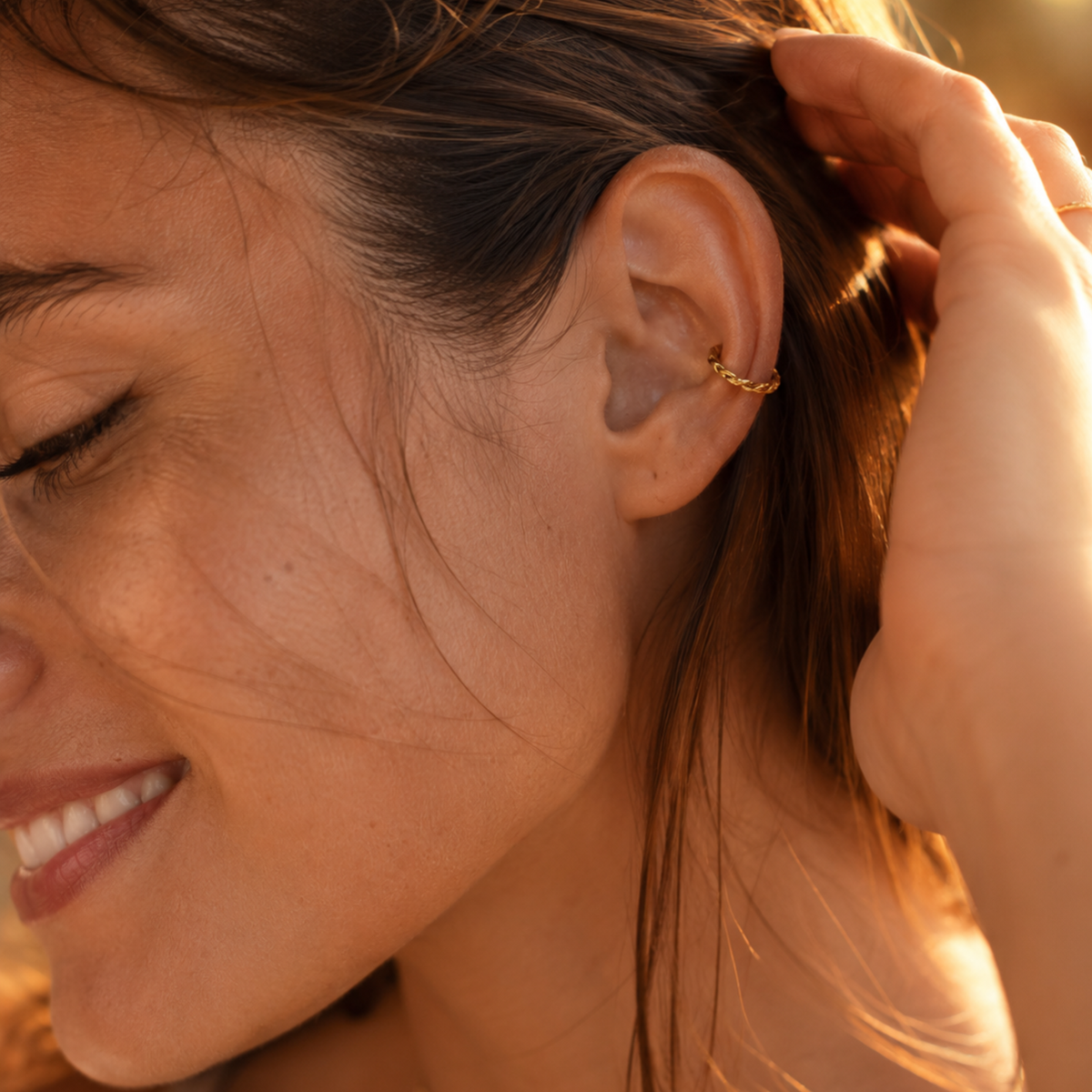 A close-up of a woman's face, with her eyes closed and her hand touching her ear.