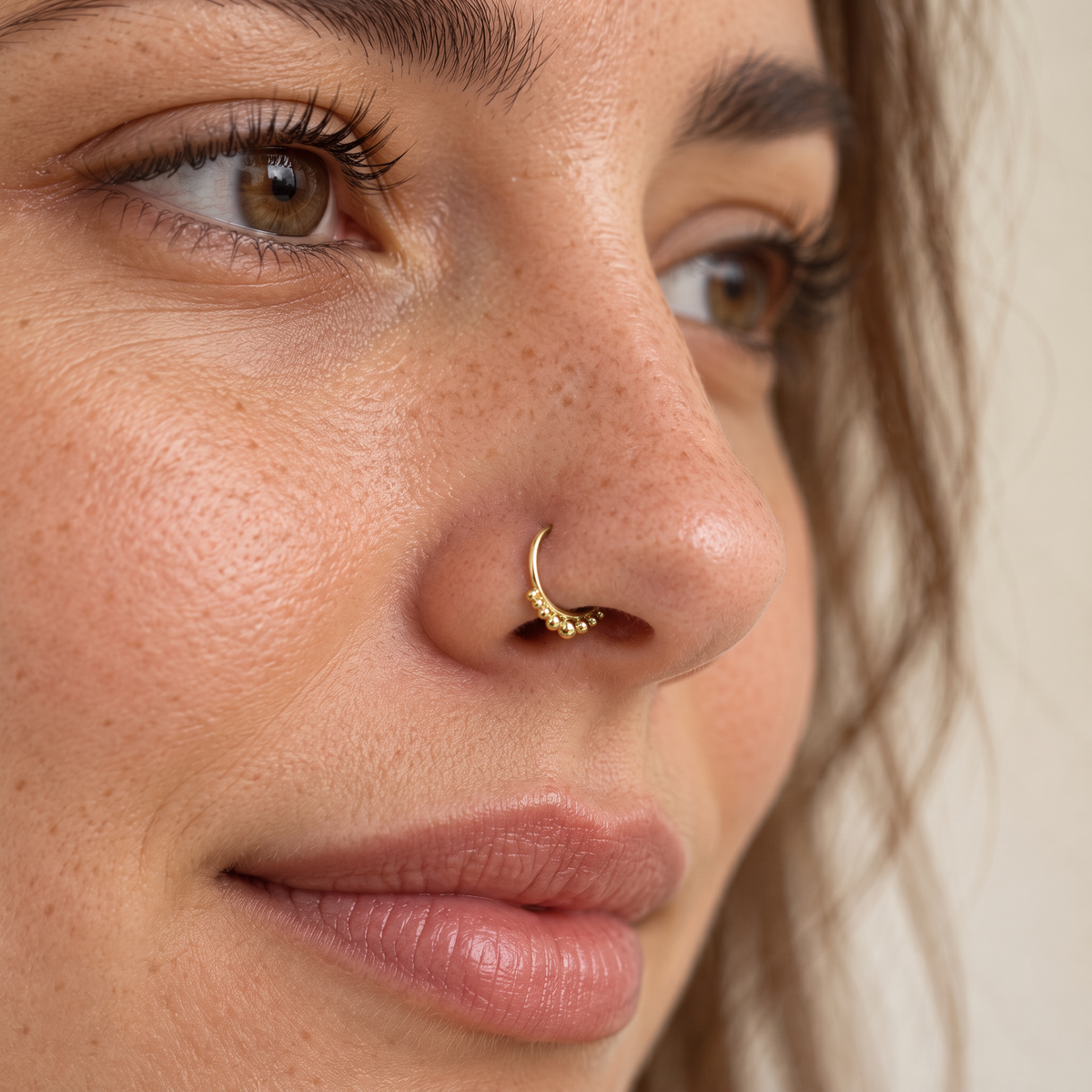 A close-up of a woman's face, focusing on her nose and lips. She has a gold nose ring and her eyes are brown.