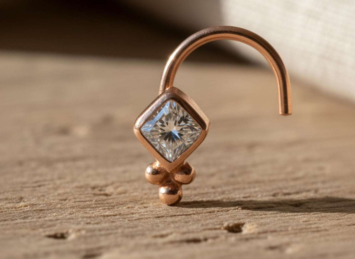 A close-up image of a diamond-shaped pendant with a clear gemstone, set in a gold-colored metal.