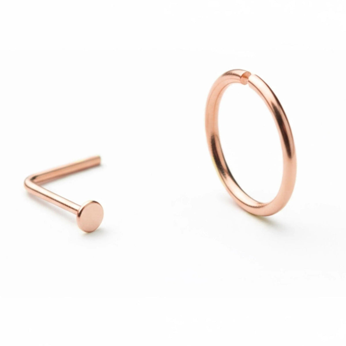 two pieces of jewelry: a small, round copper-colored nose ring and a larger, round copper-colored ring.