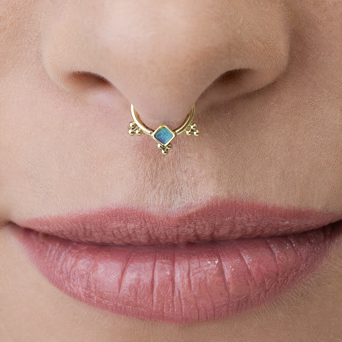 A close-up of a person's lips with a gold nose ring featuring a blue gemstone.