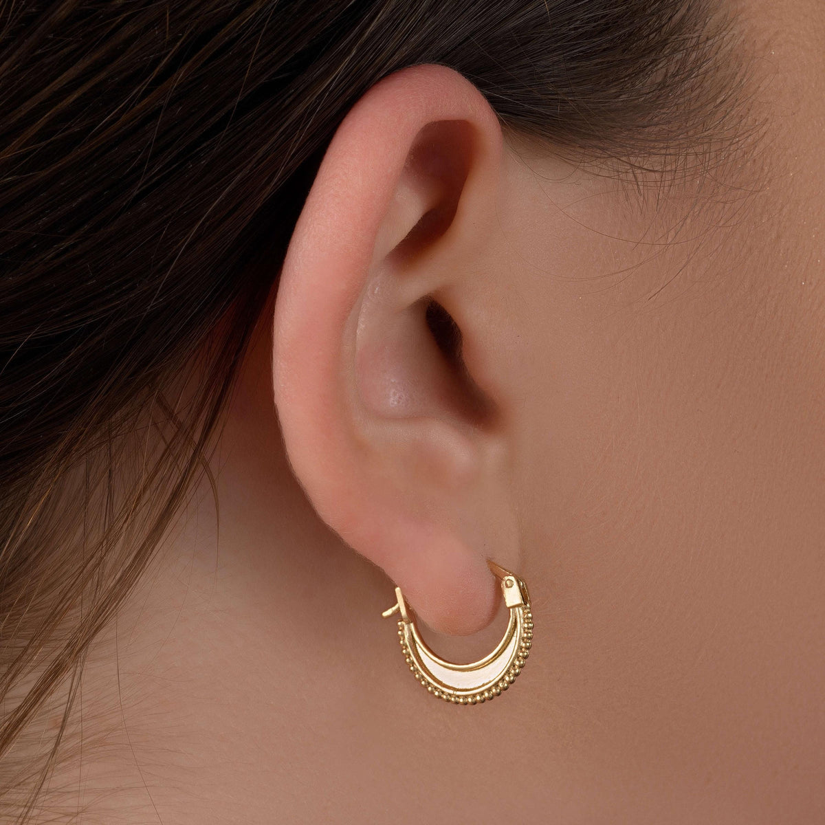Indian-Inspired Gold Hoop Earrings: A close-up view of a person's ear adorned with a gold earring featuring a decorative design.