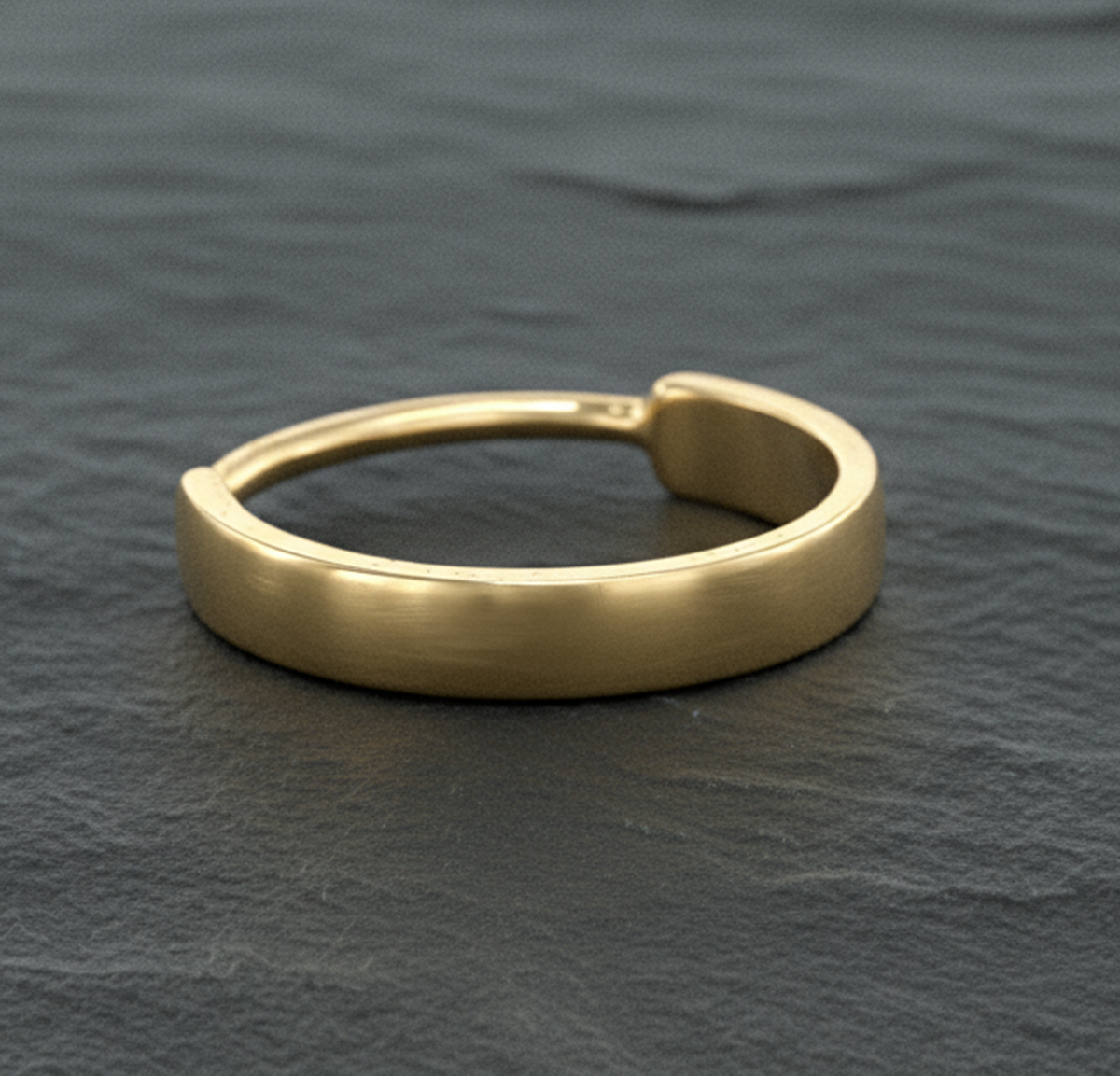 A gold ring with a curved band is resting on a dark surface.