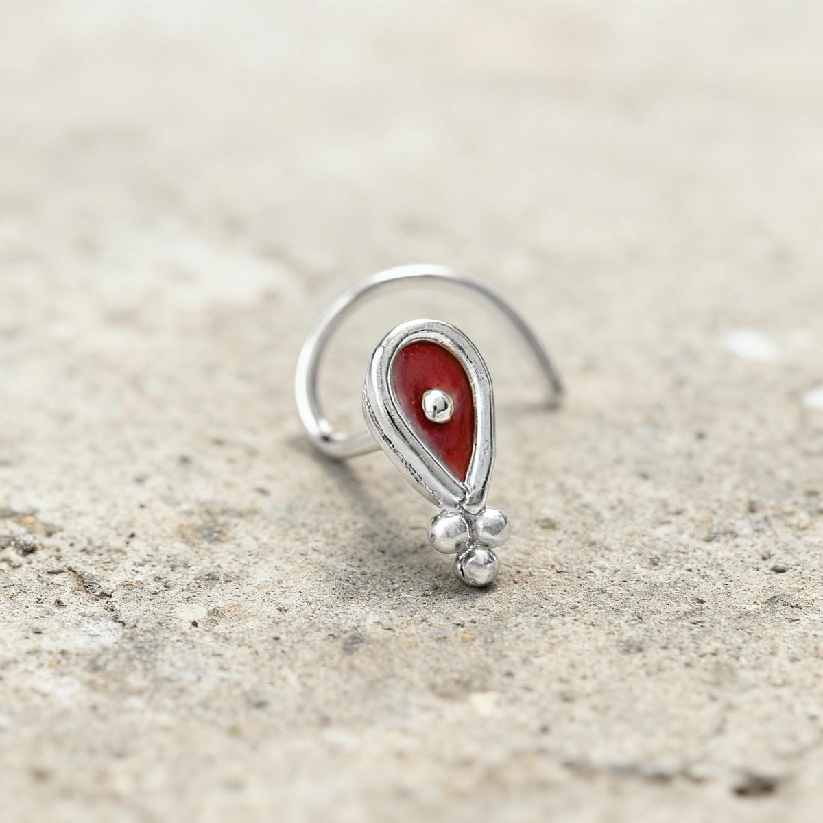 A silver earring with a red gemstone is resting on a concrete surface.