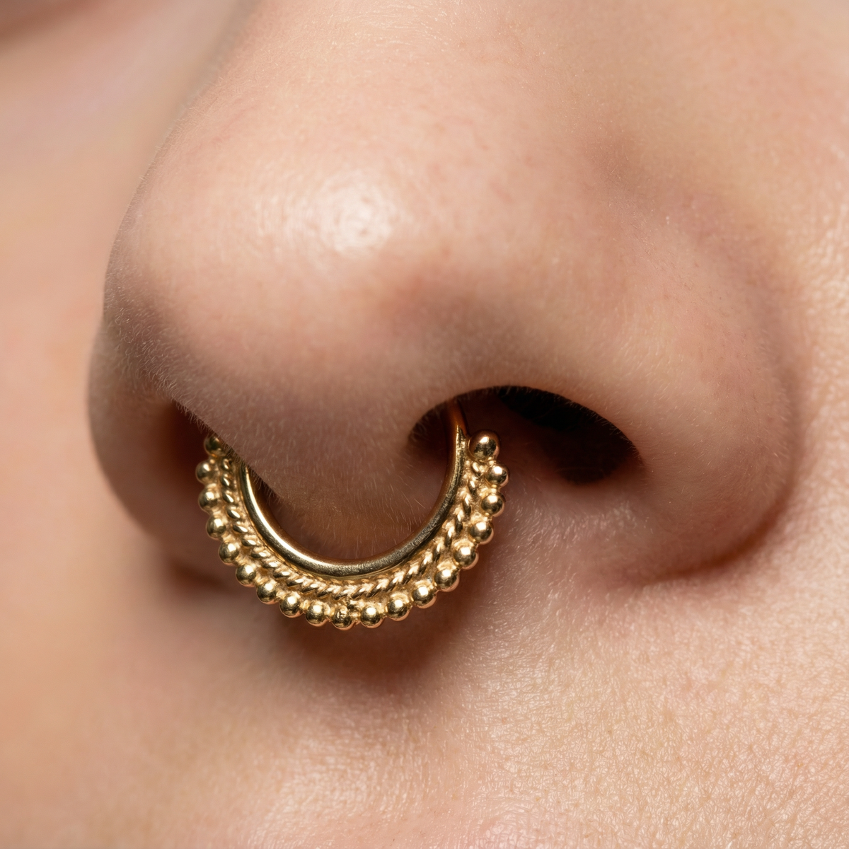 A close-up of a person's nose with a gold-colored nose ring featuring a decorative design.