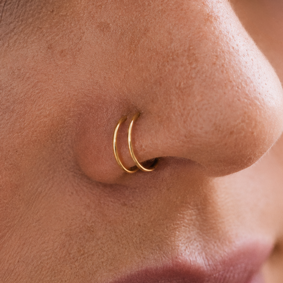 A close-up of a person's nose with a gold-colored nose ring.