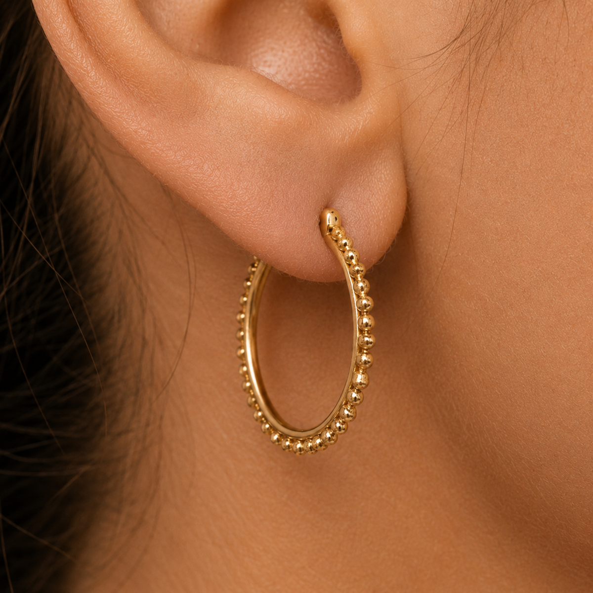 A close-up view of a person's ear adorned with a gold hoop earring featuring a decorative bezel.
