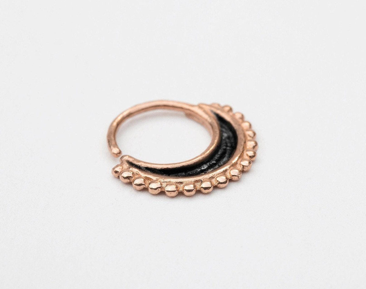 A gold-colored metal nose ring with a black accent and a decorative pattern of small beads around the edge.