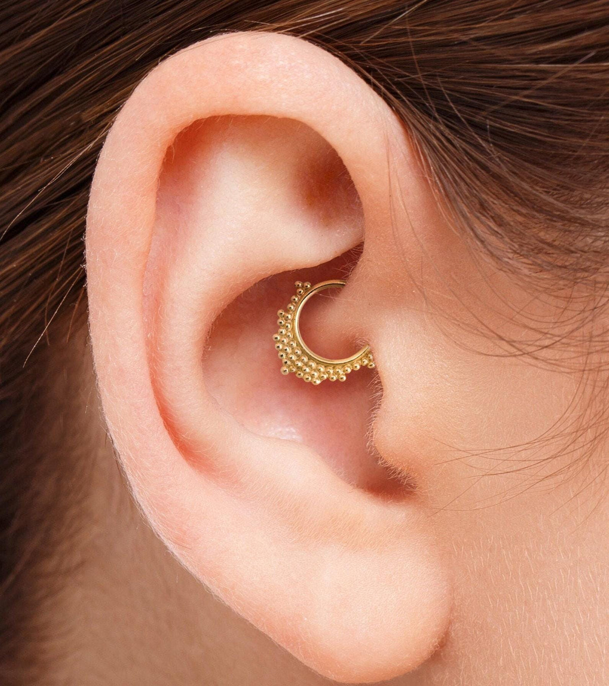 A close-up view of a person's ear with a gold-colored piercing in the earlobe.