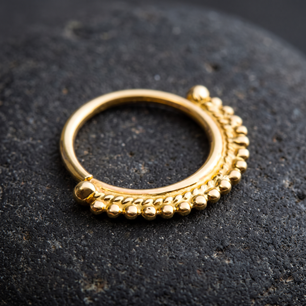 A gold-colored ring with a decorative design on a dark surface.