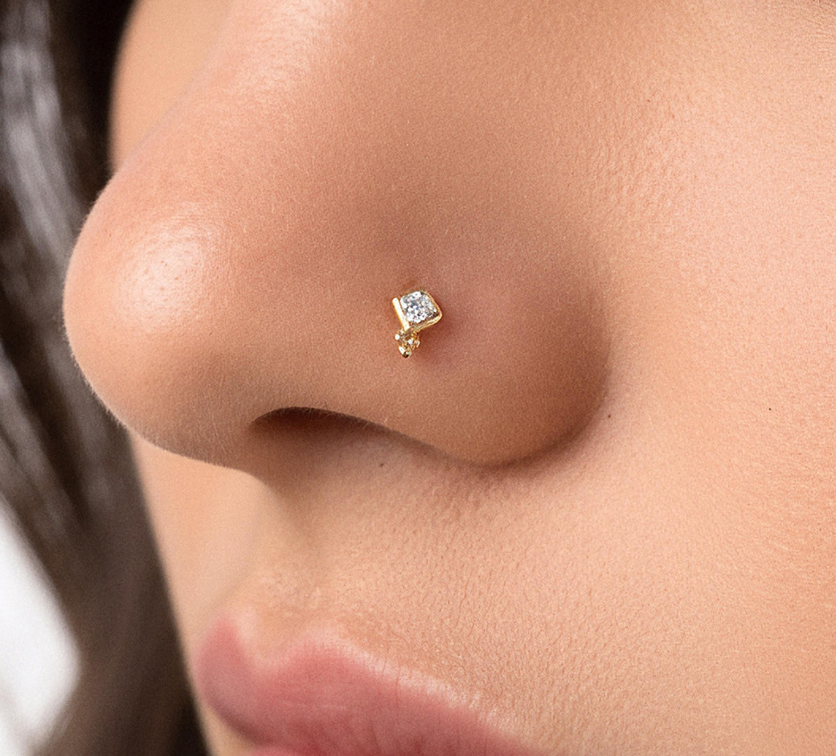 A close-up of a person's nose with a small gold nose stud featuring a diamond accent.