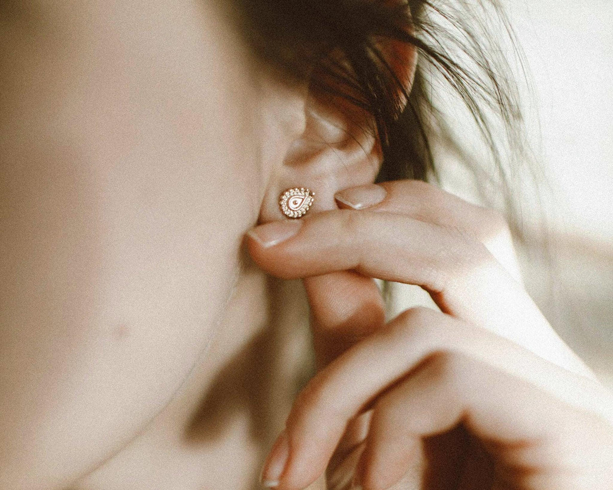 A close-up of a person's ear with a gold earring, with their hand gently touching the earlobe.