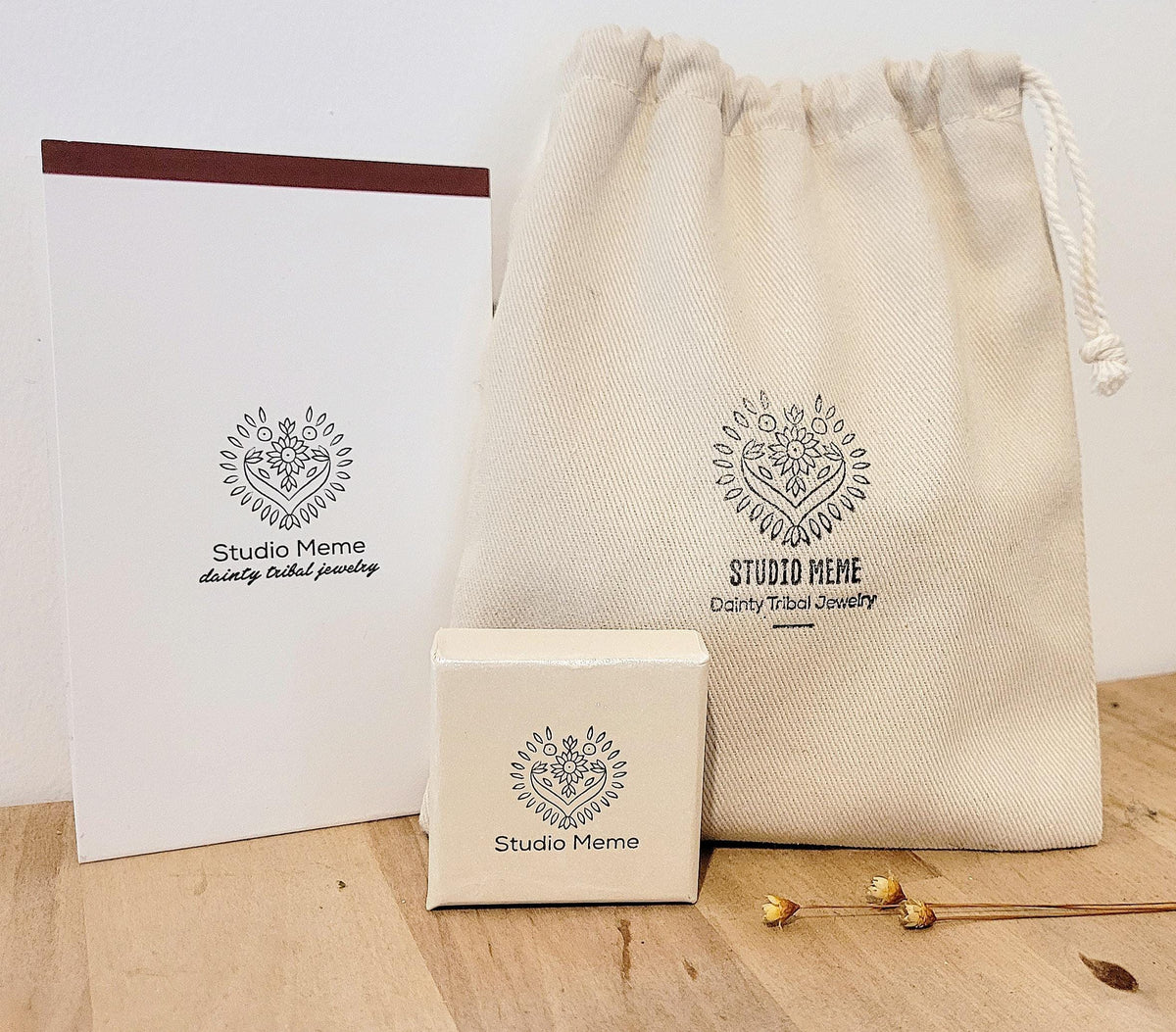 a beige drawstring bag, a small square box, and a white paper bag with the Studio Meme logo, all placed on a wooden surface.