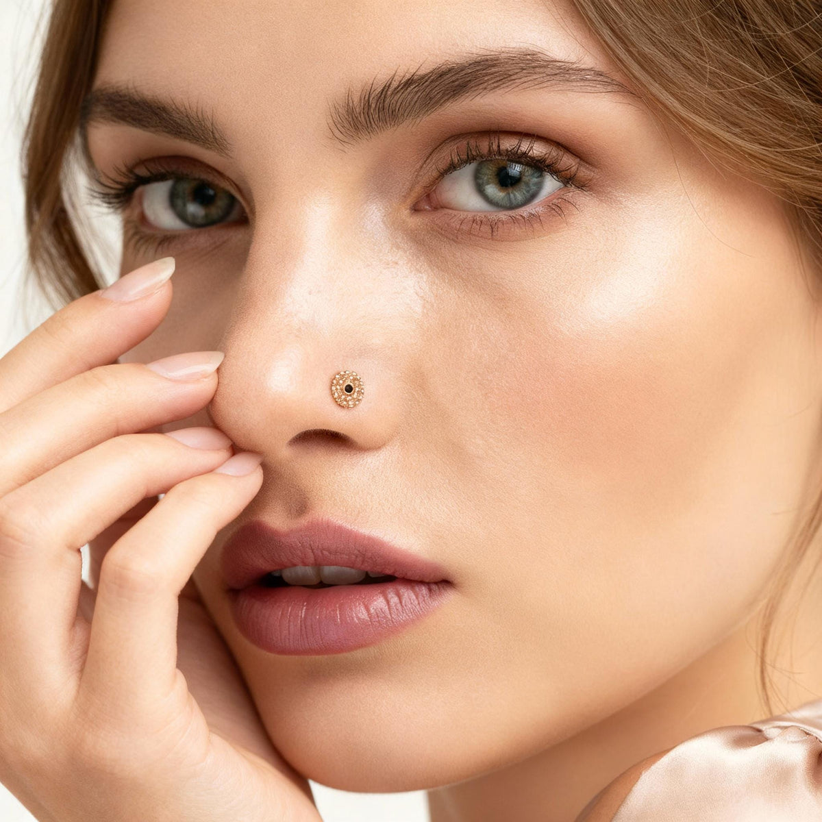 A close-up portrait of a woman with her hand on her nose, wearing a gold nose ring.
