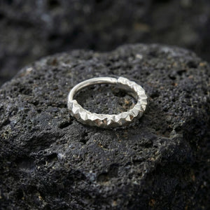 A silver ring with a unique, textured design rests on a dark, rocky surface.