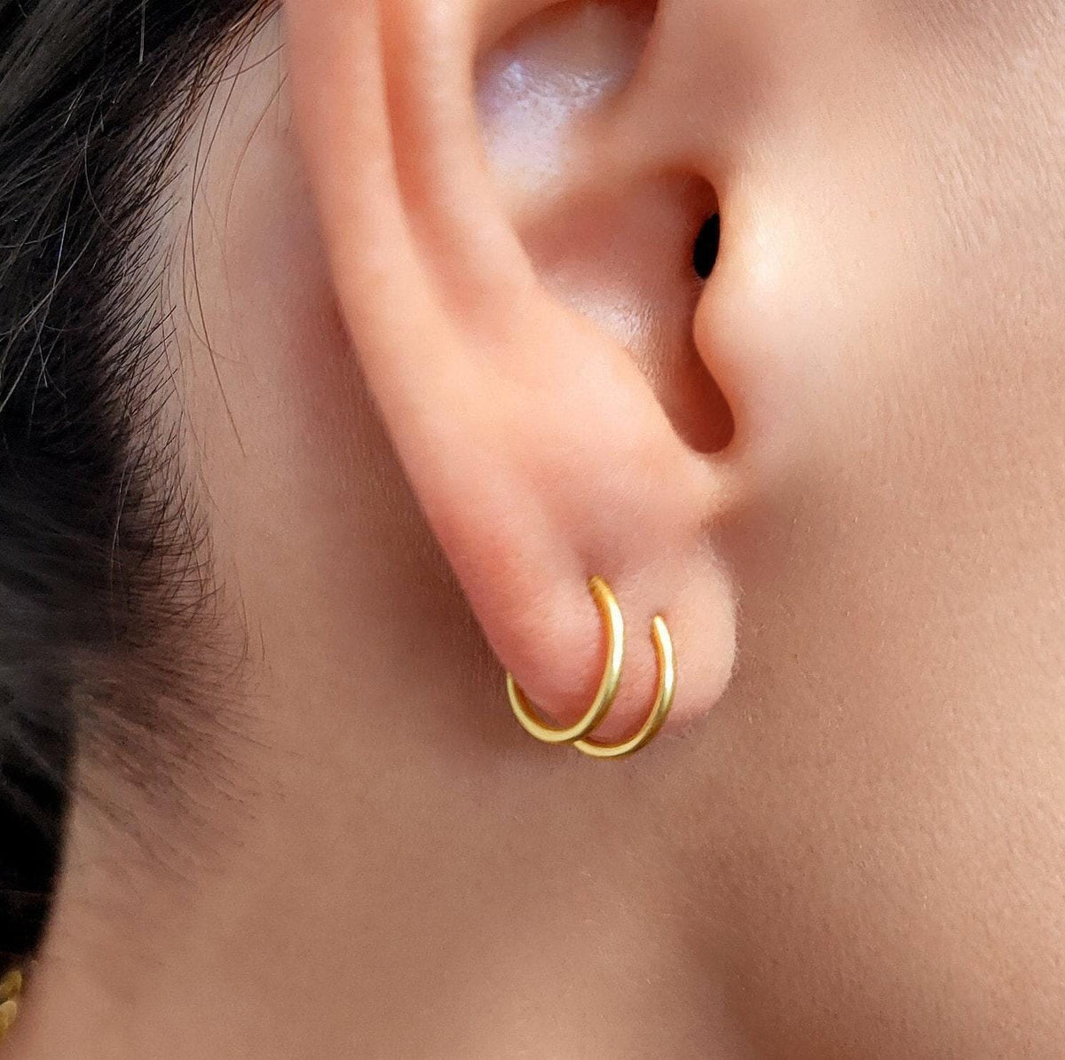 A close-up view of a person's ear with a pair of gold hoop earrings attached.