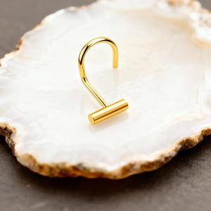 A gold-colored metal hook or earring is resting on a white, speckled surface, such as a piece of marble or a white stone.