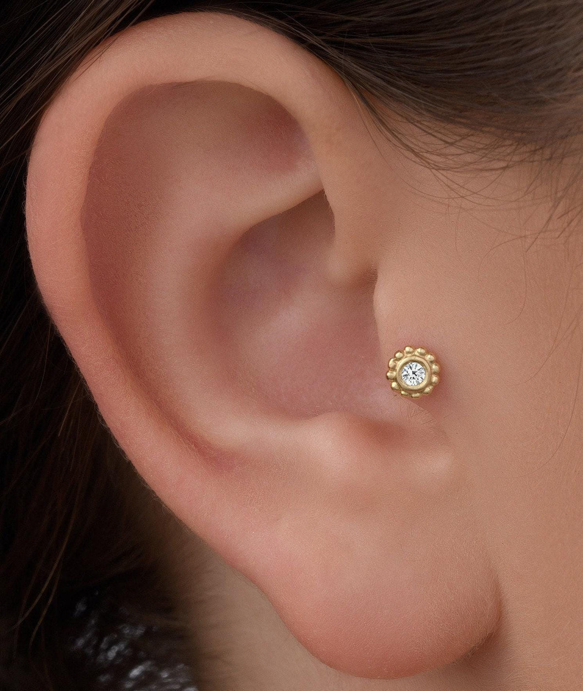 Tragus Earring: White Gold Diamond Stud. A close-up of a person's ear with a small gold earring featuring a diamond in the center.