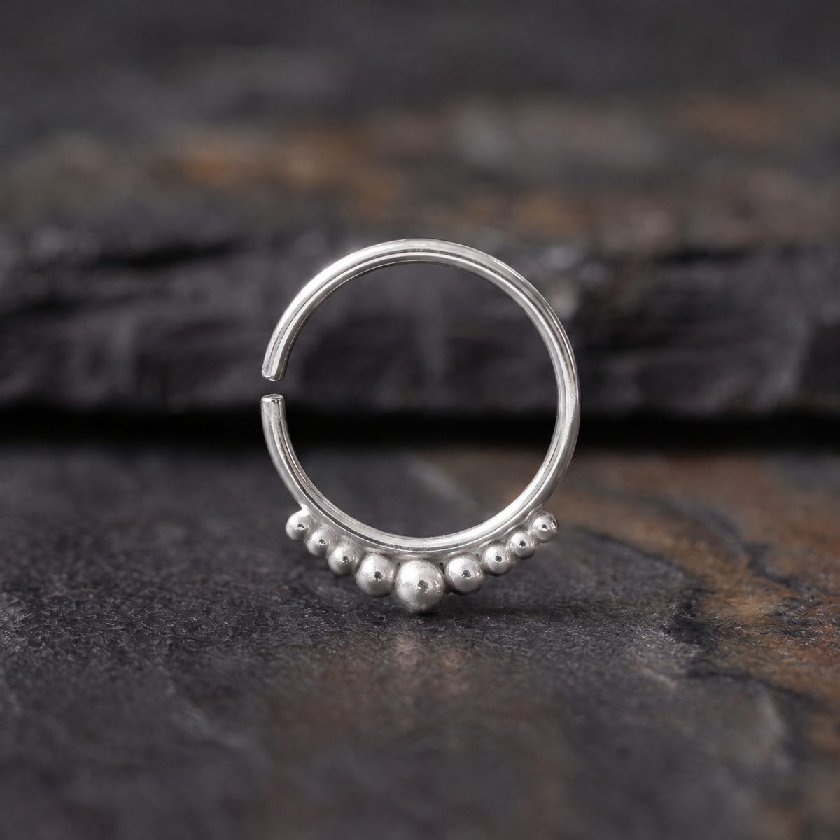 A silver hoop earring with a row of small beads on the front rests on a dark surface.