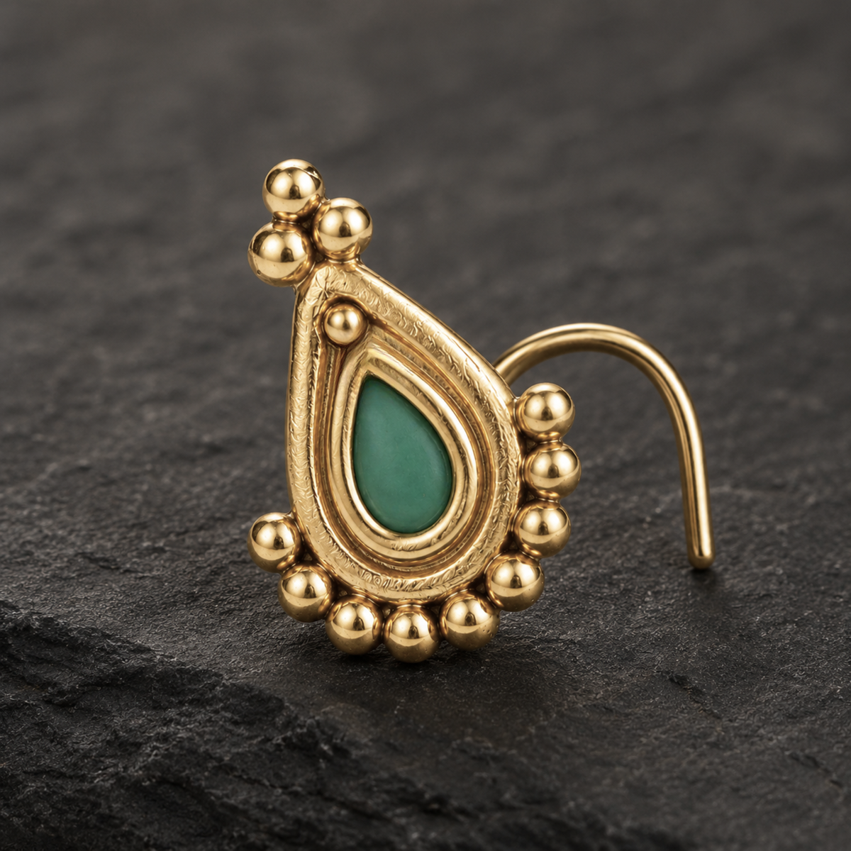 A gold-colored nose ring with a green gemstone in the center, set against a dark background.